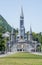 Cross and  the Basilica of the Holy Rosary in Lourdes, France. Main facade of the Sanctuary at Lourdes