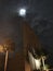 Cross of church appears to light up as full moon shows itself from beyond clouds.