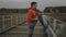 Cross country runner warming up and muscle stretching before training outdoors on wooden bridge in national park in cold