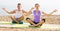 Cross-legged couple practice yoga on beach in morning