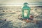 Cross-processed lantern on beach with shells and rope at sunrise