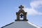 Cross symbol with bell on rooftop of church rising up in sky