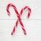 Crossed peppermint candy canes on white wooden background, top view, square