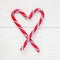 Crossed peppermint candy canes on a white wooden background, top view, square format