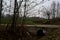 Crossing between a dirt trail and a paved one next to a stream of water on a cloudy day in the italian countryside