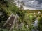 Crossover bridge on the river surrounded by greens and trees under the cloudy sky in the park