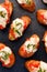 Crostini, toasts, grilled baguette slices dwith tomatoes, mozzarella cheese and fresh basil on a black background, top view.