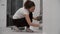 Crouching young woman paints brick wall in gray using brush