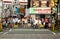 A crowd of Japanese pedestrians wait at a railroad crossing beneath colorful signs.