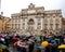 Crowd with multi color umbrellas is standing near Trevi fountain.