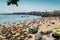 Crowded Duquesa beach on a hot summer`s day, with the town of Cascais in the background including the ancient fort