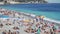 Crowded public beach at seashore, many people sun tanning or splashing in water