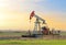 Crude oil pump jack at oilfield on sunset backround. Fossil crude output and fuels oil production. Oil drill rig. Crude mining