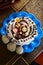Cruffin on a blue plate white glazing decoration with nuts and sugar flowers, top view, closeup