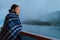 Cruise ship passenger on Alaska travel vacation enjoying scenery at dusk on suite balcony deck with wool throw in cold