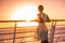 Cruise ship vacation woman travel watching sunset at sea ocean view. Elegant lady in white dress relaxing on deck balcony, luxury