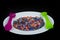 Crushed multicolored plastic pieces on white plate and green spoon and lilac fork .