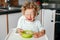 Crying Caucasian kid boy sitting in high chair with cereal puree on plate. Child refusing eat healthy food. Toddler screaming in