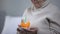 Crying elderly woman blowing out candle on birthday cake, loneliness in old age
