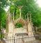 The crypt in which lies a man of high rank. Above it is a lot of columns. Around the green trees and grass.