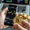 Cryptocurrency scene Hand holds Bitcoin, smartphone displays stock chart in cafe