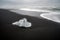 Crystal clear ice chunks washed up on the black lava sand by the waves on diamond beach in Jokulsarlon glacier lagoon.