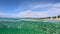 Crystal clear sea water in Sitonia, Halkidiki, Greece. Half underwater slow-motion view of sandy beach bottom, blue sky