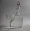 Crystal glass patterned pitcher decanter with vodka and a glass on a thin leg with vodka on a white background