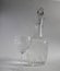 Crystal glass patterned pitcher decanter with vodka and a glass on a thin leg with vodka on a white background
