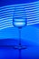 Crystal glass with pure water painted against the light-painted background. Studio shot, blue tones, surface reflections. Still
