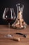 Crystal red wine glass, bottle, corkscrew, opener, sommelier knife, transparent decanter, corks on wooden table. Closeup, vertical