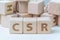 CSR, Corporate Social Responsibility concept, wooden cube block with letters forming acronym CSR on white gridline notebook,