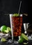 Cuba Libre cocktail in highball glass with ice and lime peel on bamboo stick with straw and fresh limes on black background