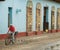 Cuban man in red shirt riding bicycle past wrought iron doorways in streets of Trinidad, Cuba