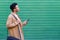 Cuban young man looking forward using his smartphone near green blinds.