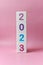 Cube tower with colorful numbers 2023 in center of the photo on pink background. New year, calendar.