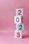 Cube tower with colorful numbers 2023 in center of the photo on pink background. New year, calendar.