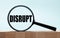 Cubes on a light blue wooden background. On them a magnifying glass with the word DISRUPT