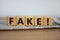 Cubes placed on a newspaper form the word `fake`. Beautiful wooden table. White background. Business concept. Copy space