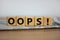 Cubes placed on a newspaper form the word `oops`. Beautiful wooden table. White background. Business concept. Copy space