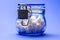 Cubes of white sugar in a transparent glass jar with a lid closed on a lock, on a blue background. Concept of proper