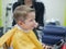 Cucasian brunet toddler on the haircut with a professional children\\\'s hairdresser. Little boy having a stylish haircut