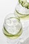 Cucumber infused detox water in glasses with ice. Homemade flavored lemonade on white gray background close up