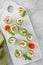 Cucumbers rolls with cream cheese, salted salmon and fresh herbs served on a white ceramic board on a concrete background.