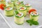 Cucumbers rolls with cream cheese, salted salmon and fresh herbs served on a white ceramic board on a concrete background.