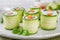 Cucumbers rolls with cream cheese, salted salmon and fresh herbs served on a white plate on a concrete background. Selective focus