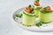 Cucumbers rolls with soft cheese, pieces of salted salmon, microgreens and black sesame served on a white plate. Holiday vegetable