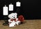 Cudlely teddy bear with red bow tie, red rose, white candles perched on black candle holders on mesh place mat and wooden table wi