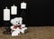 Cudlely teddy bear with red bow tie, white candles perched on black candle holders on mesh place mat and wooden table with card an