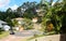 Cul-de-sac in Queensland Australia suburb with houses up on hills with steep driveways and tall gum trees behind and tropical land